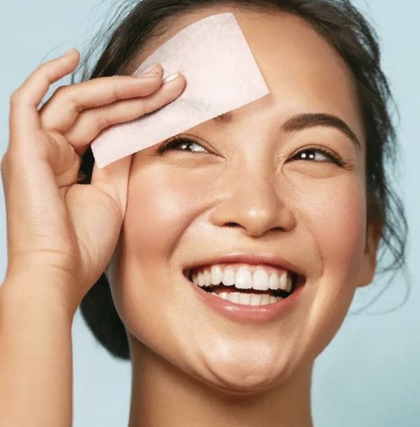 una donna tampona sul viso una salvietta assorbi-sebo prima del refresh make-up